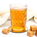 A jar of homemade whiskey with caramel and caramel candies on a white surface