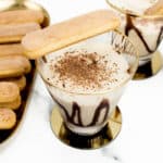 A tray of lady finger desserts sits to the left of two Tiramisu Martinis garnished with chocolate shavings and a lady finger