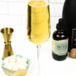 A glass of champagne sits next to a teal and gold bowl of sugar cubes and bitters.