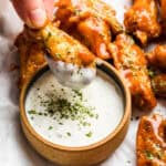 A hand dips an air fried chicken wing into a bowl of ranch.