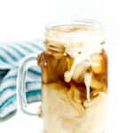 Milk and coffee swirl together among ice cubes in a mason jar glass with a handle.