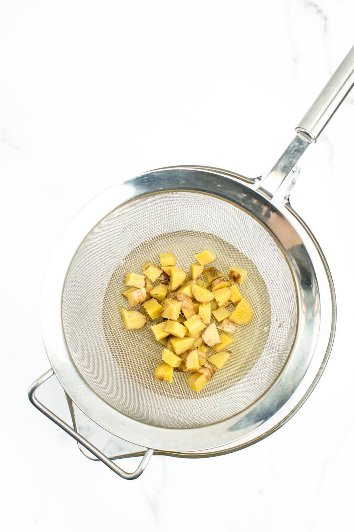 a sieve straining out fresh ginger from ginger ale concentrate
