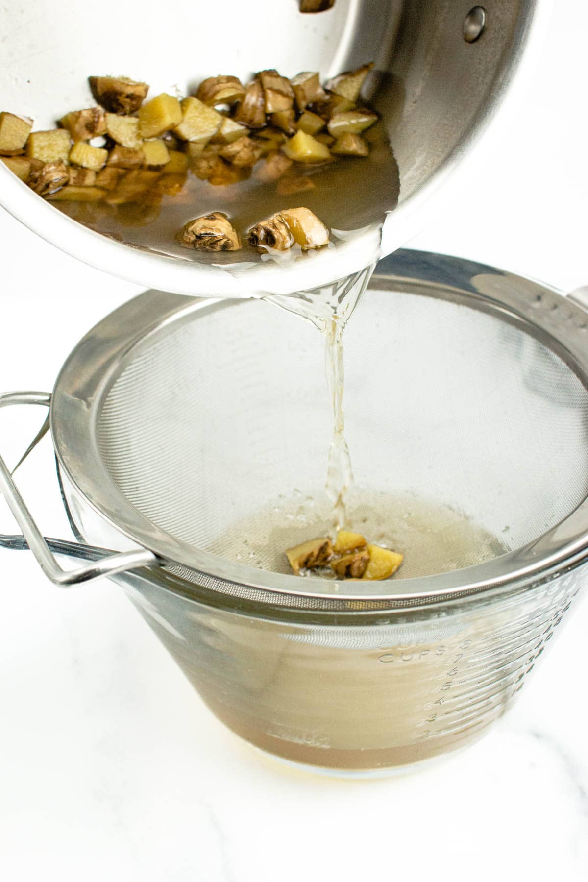 pouring ginger root and ginger liquid into a fine-mesh strainer