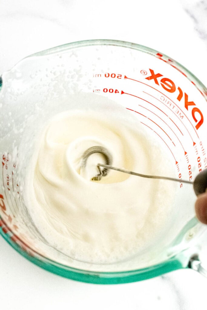 A coffee foamer is used to create foam in a glass measuring cup.