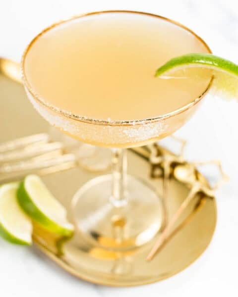 A bubbly champagne drink on a gold tray with lime wedges.