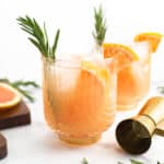 Two greyhound cocktails garnished with grapefruit slices and sprigs of sage.