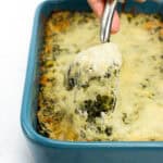 A creamy spinach dip is spooned out of a blue baking dish.