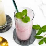 An overhead view of a creamy pink soda drink with mint and a gold spoon laying beside.