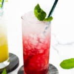 A cranberry Italian soda garnished with a mint sprig on a gray stone coaster.