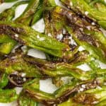 a closeup of blistered shishito peppers with flaky sea salt.
