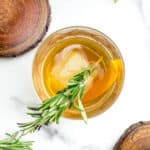 A classic whiskey cocktail sits beside wooden coasters and herb sprigs.