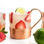 Two strawberry mules next to a sliced strawberry and whole lime.