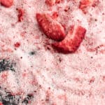 Pieces of dried strawberries mixed in with granulated sugar on a black surface.
