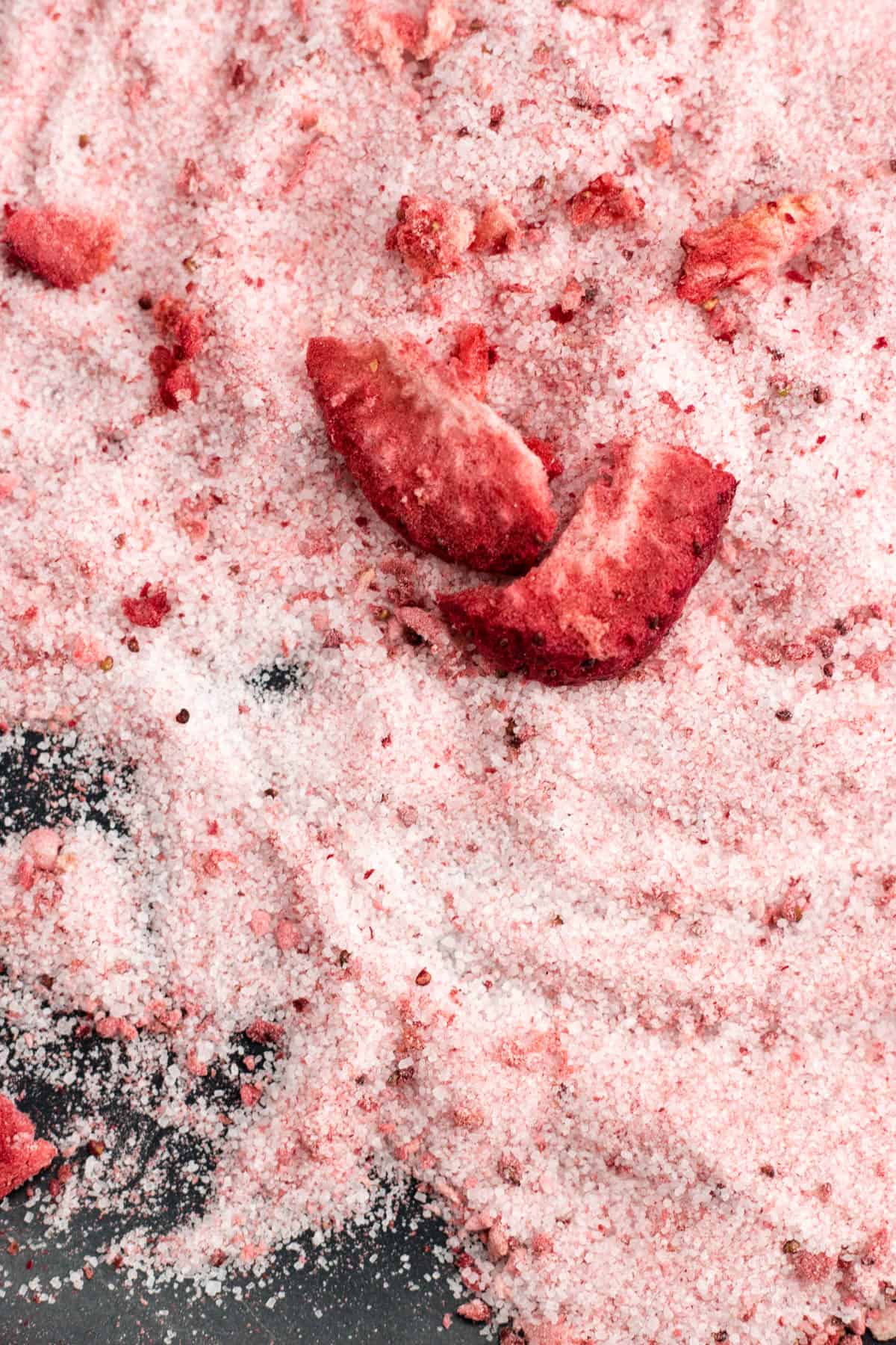 Pieces of dried strawberries mixed in with granulated sugar on a black surface.