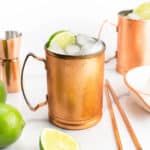 Half of a lime sits in front of vodka cocktails in copper mugs.