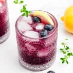 A blueberry drink in a glass alongside whole blueberries.