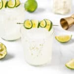 Two margarita glasses with limes and garnishes.