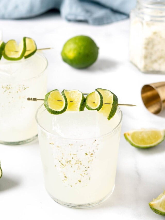 Two margarita glasses with limes and garnishes.
