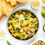 A bowl of chips and halves of spent limes sit near two bowls of pineapple-based salsa.