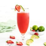A strawberry agua fresca with limes and strawberries on a white background.