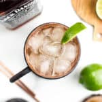 An overhead view of a cocktail with ice garnished with a lime wedge alongside mule ingredients.