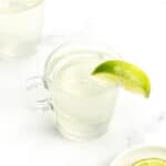 An overhead view of two cups of white tea shots garnished with lime wedges.