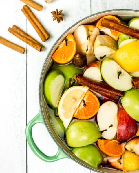 A pot filled with apples, cinnamon sticks, and oranges.