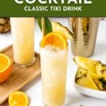 A tall glass of Painkiller drink garnished with an orange slice, pineapple wedge, and grated nutmeg, surrounded by fresh fruit and a gold cocktail shaker.