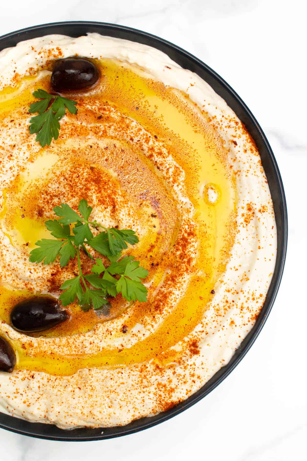 A bowl of feta dip with olives and parsley.