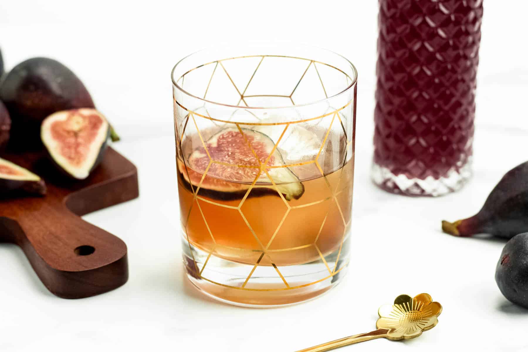 A fig old-fashioned cocktail with a rich amber color and citrus garnish.
