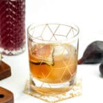 A glass of a cocktail with figs and a gold spoon.