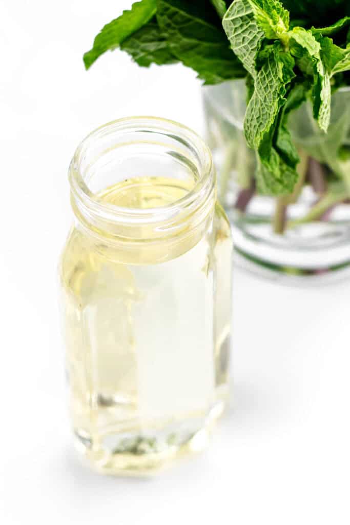 A bottle of liquid simple syrup next to a glass of mint.