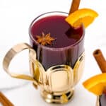 Mulled wine in a gold cup with cinnamon sticks and orange slices.