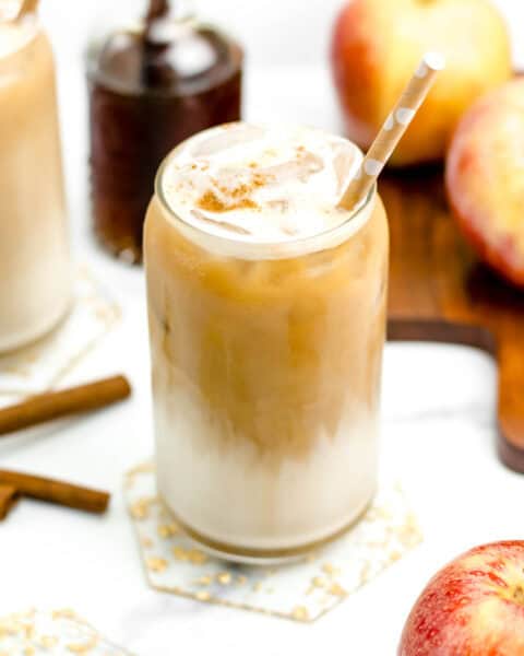 Two mugs of iced Apple Crisp Macchiato coffee with apples and cinnamon.