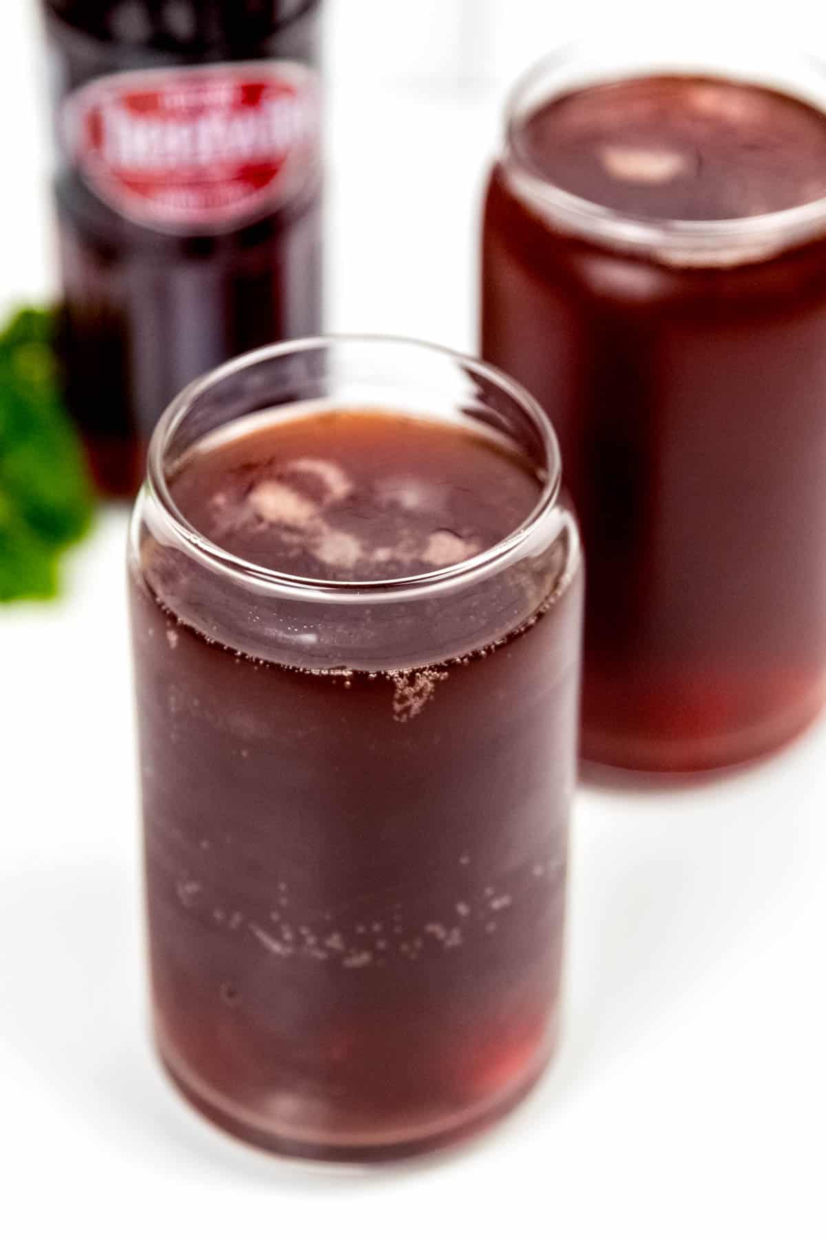 Two glasses with a drink and a bottle of coca cola.