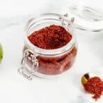 A glass jar with red chili powder and limes.