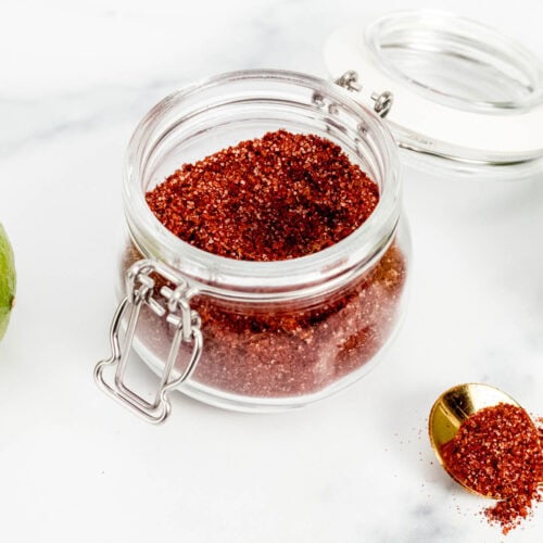 A glass jar with red chili powder and limes.