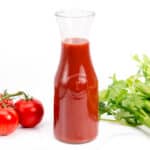 A bottle of Clamato Juice next to celery and tomatoes.