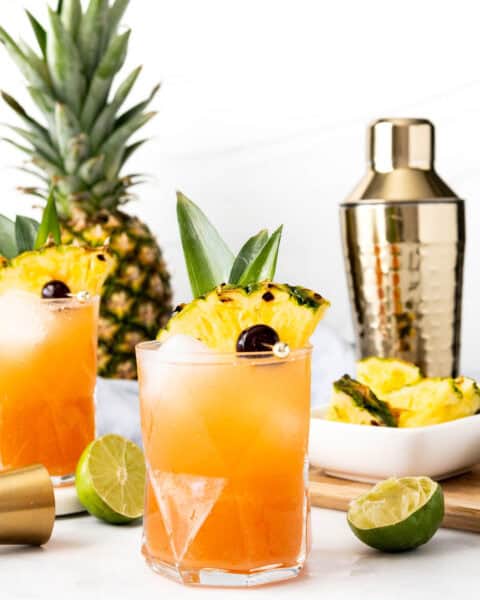 A refreshing Jungle Bird Drink with pineapple and cherry garnishes on a white table.