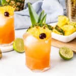 Two Jungle Bird Drinks with pineapple and lime garnishes on a table.