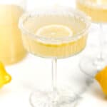 Two glasses of lemonade with a bottle of lemon juice.