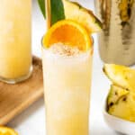 A cocktail with orange slices and pineapples on a wooden cutting board.