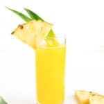 A glass of pineapple juice with slices of lime and pineapple, topped with refreshing slices of Pineapple.
