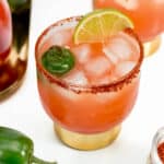 Two Vampiro drinks with limes and peppers on a tray.