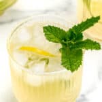 Two glasses of lemonade with mint leaves in them.