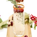 Two glasses with cranberries and sprigs of rosemary on a gold tray.