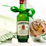 A bottle of Jameson whiskey paired with boozy hot chocolate bombs, garnished with marshmallows and tied together with a green ribbon.