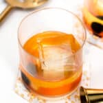A glass of a Scotch cocktail with ice and a spoon.