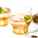 Two tequila old fashioned cocktails with a gold rimmed glass, ice, and lime.