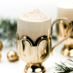 Two festive eggnog mugs with whipped cream and cinnamon sticks.